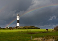 Der Leuchtturm in Kampen auf Sylt mit Regenbogen am Horizont kurz nach einem Gewitterschauer
