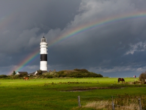 Der Leuchtturm in Kampen auf Sylt mit Regenbogen am Horizont kurz nach einem Gewitterschauer
